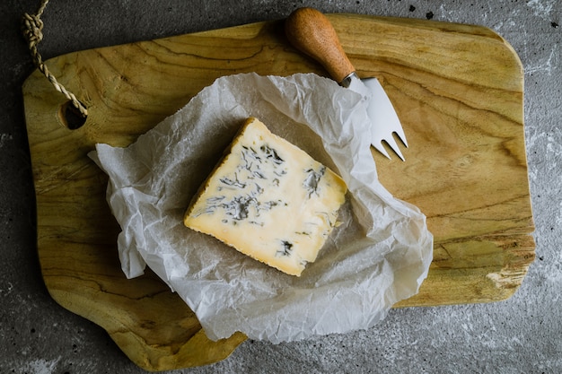 Slice of blue cheese on wooden board with cheese knife