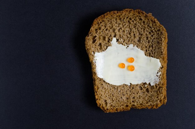 A slice of bread anointed with oil and red caviar on black background