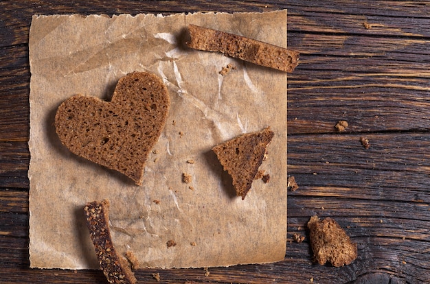 Slice of bread in a heart shape on crumpled paper on an old wooden table