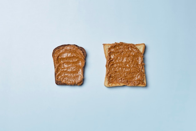 Slice of brown bread and a toast buttered with tasty peanut butter over the blue surface