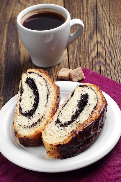 Slice bun with poppy and cup of coffee on wooden table