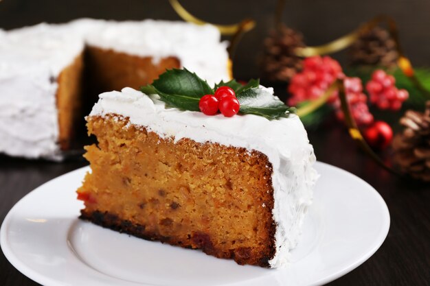 Кусочек торта покрытый кремом с рождественским украшением на поверхности деревянного стола