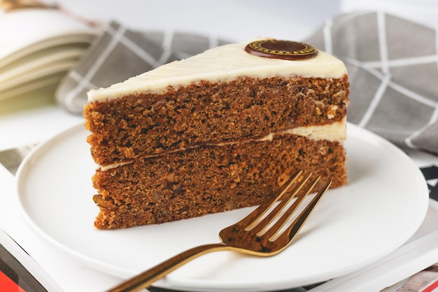 Photo slice of carrot cake on a white plate with a book in the background