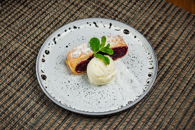 A slice of cherry strudel with vanilla ice cream and a mint sprig on a white plate