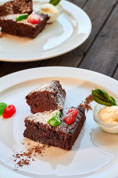 Slice of chocolate cake with candied fruit, mint and ice cream on a plate