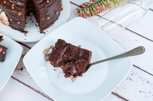 Кусочек шоколадного торта с начинкой из темного ганаша рядом с вилкой сверху