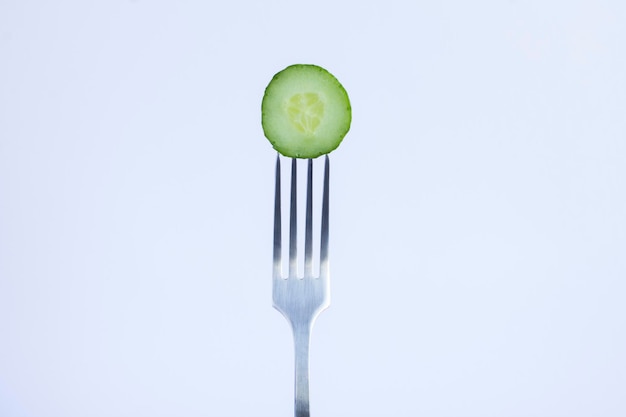 Slice of cucumber stabbed on a silver fork on the white background Closeup Copy space