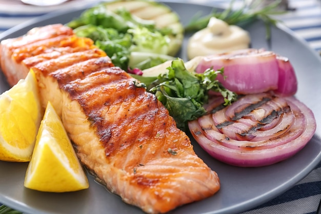 Slice of delicious salmon with vegetables on plate close up