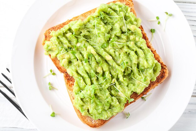 A slice of fresh bread on a plate with avocado on a background of light wooden boards