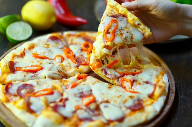 Una fetta di pizza fresca calda con una striscia di mozzarella in mano.