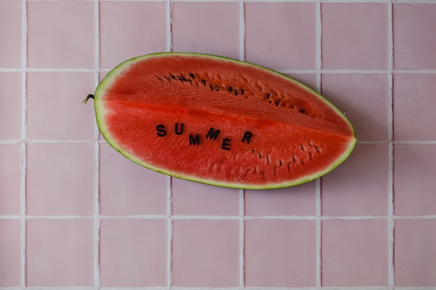 A slice of a fresh juicy red watermelon with black letterssummer on a pink tile kitchen countertop.