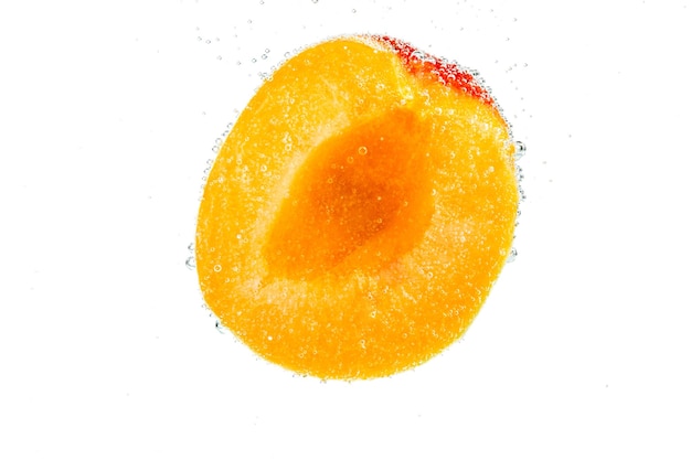 Ломтик свежих спелых абрикосов падает в воду с пузырьками на белом фоне