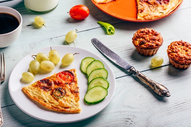 Slice of frittata with cup of coffee, grapes and muffins over light wooden background. Healthy eating concept.