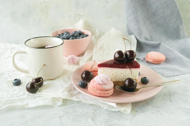 Кусочек фруктового торта со сливками на тарелке, украшенный ягодами, чашка кофе