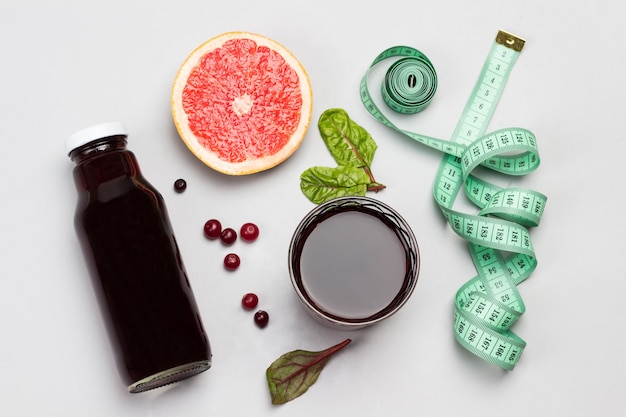 Slice of grapefruit, cranberries, juice in glass and in bottle, measuring tape. Flat lay. Copy space
