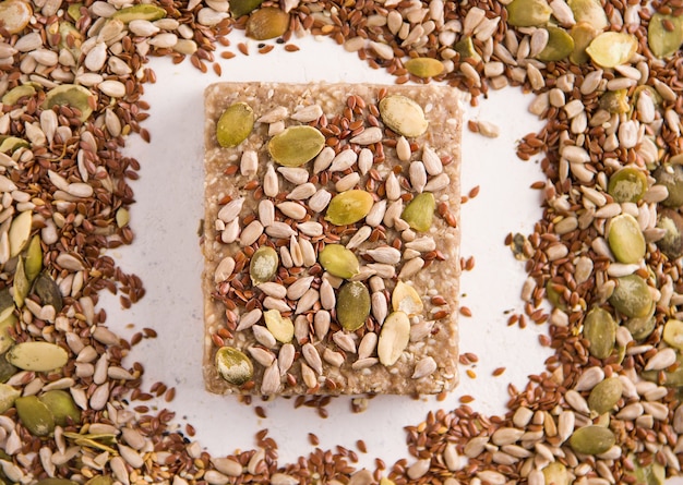 A slice of halva on a white background next to different seeds. View from above