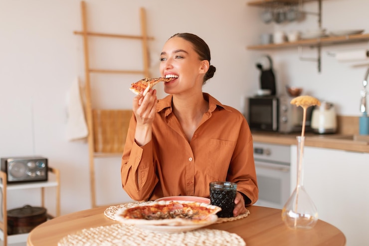 Photo 幸せのスライス 幸せな若い空腹の白人女性がキッチンのテーブルに座って美味しい食べ物を食べています
