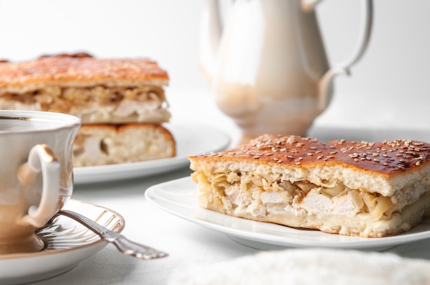 A slice of homemade chicken and sesame pie On a white plate Near a coffee pot and a cup of coffee White background Closeup