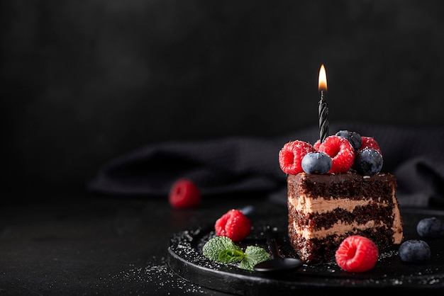 Fetta di torta al cioccolato artigianale con frutti di bosco freschi e candela di compleanno, primo piano