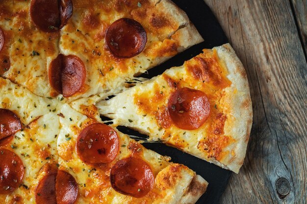 Photo a slice of hot italian pizza with stretching cheese pizza pepperoni on a dark wooden background