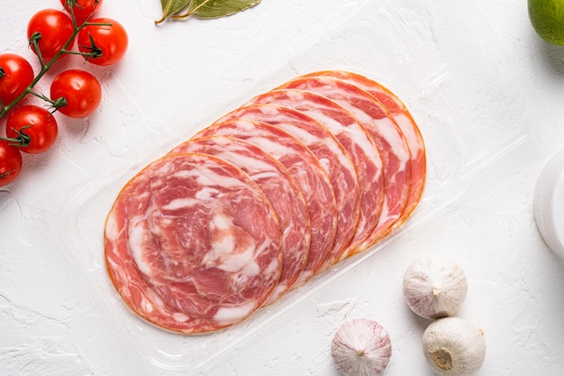 イタリアのハムと肉のスライス真空パッケージセット、白い石のテーブルの背景、上面図フラットレイ