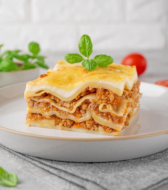 Slice of lasagna bolognese with meat sauce and bechamel with\
melted cheese on top and fresh basil