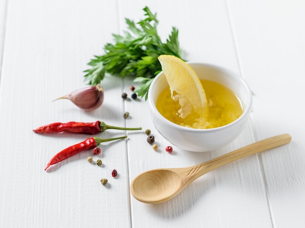 Una fetta di limone in una tazza con olio d'oliva, pepe e aglio e cucchiaio di legno su un tavolo bianco. condimento per insalata dietetica.