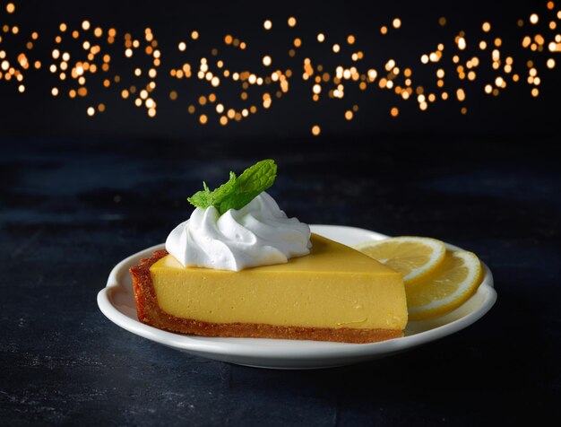 Slice of lemon tart on white plate on holiday lights background