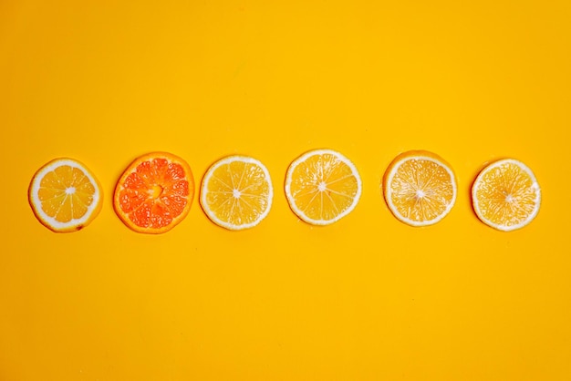 Slice of lemons and orange fruit arranged in a line on yellow background