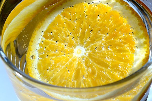 a slice of orange covered with bubbles lies in a glass of sparkling water. Close-up.