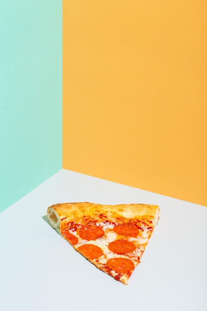 Кусочек пиццы пепперони оранжевый серый бирюзовый бумажный фон современное фото высокого качества