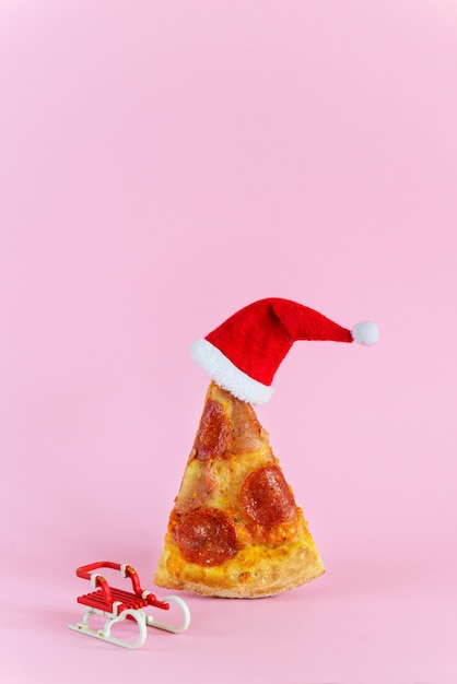 Slice of pepperoni pizza with santa hat and sleight beside