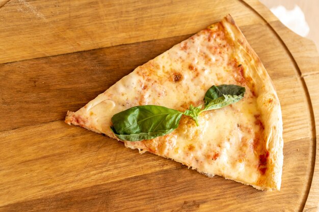 Photo slice of pizza margherita with mozzarella and basil leaves on wooden stend traditional italian food