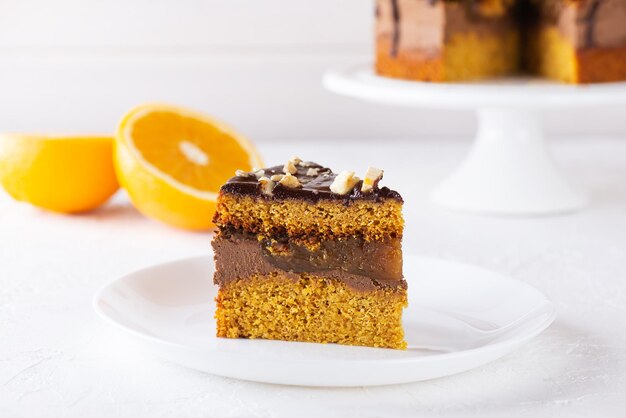 A slice of pumpkin pie with orange, chocolate and nuts on a white plate. Sugar, gluten and lactose free, vegan.