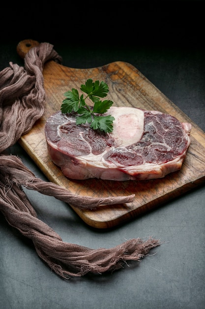 Slice of raw beef shank on a cutting board on dark