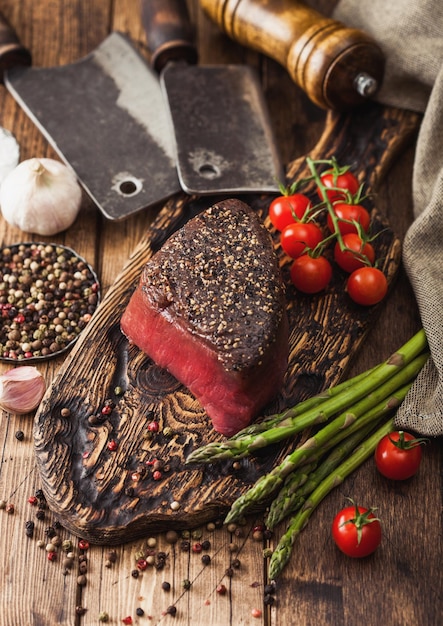 生の牛肉の上面のスライスと塩とコショウを木製のまな板に、肉の手斧、ニンニク、アスパラガスのチップを木製のキッチンテーブルに載せます。