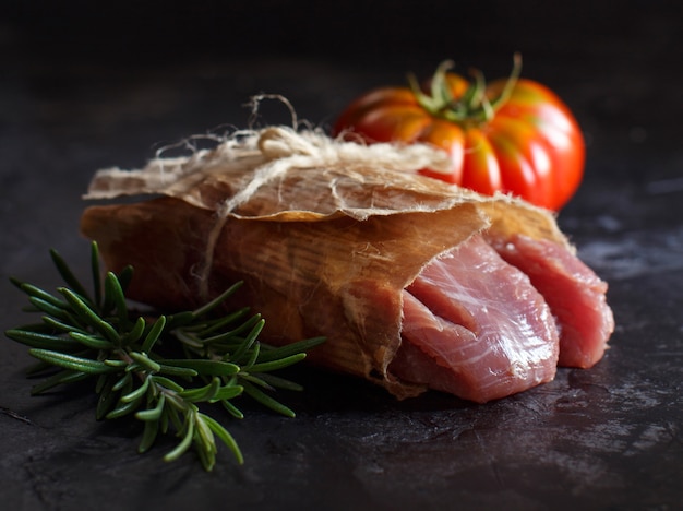 Foto fetta di bistecca di tacchino crudo con rosmarino e pomodori sul tavolo scuro