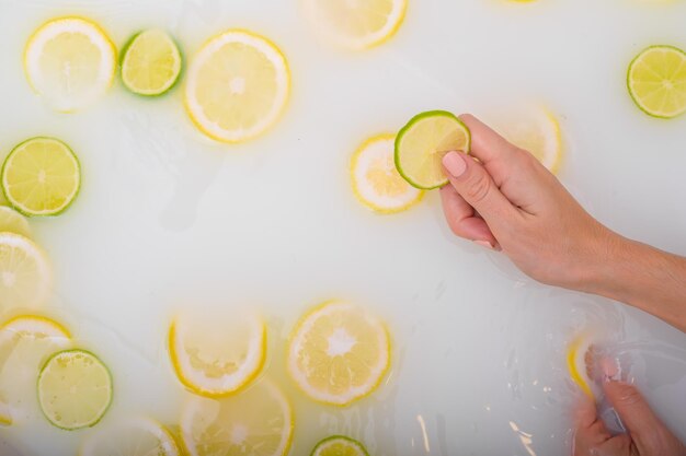 A slice of ripe lime in the hands of a woman Top view Girl takes a milk bath with lemons Citrus spa Body care Skin whitening