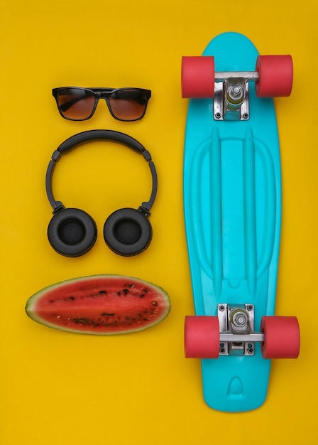 Slice of ripe watermelon and hipster youth accessories, cruiser board on a yellow background. Summer fun. Top view