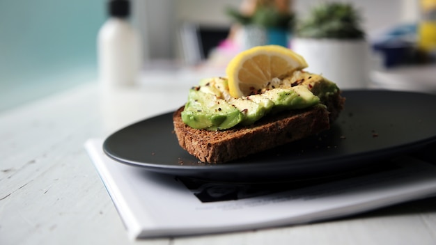 A slice of rye bread with pieces of avocado and a slice of lemon