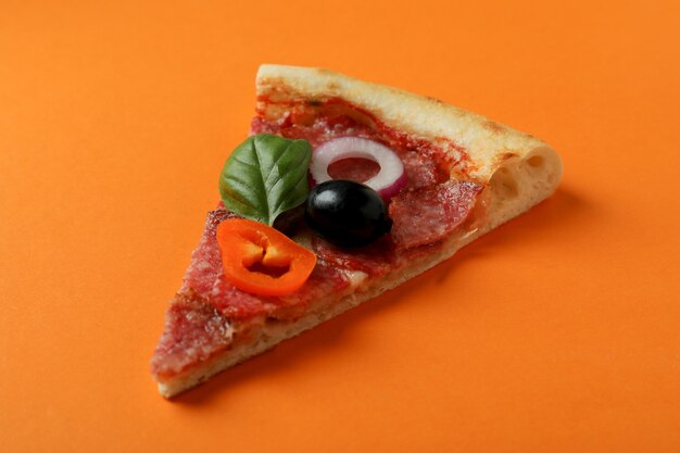 Slice of Salami pizza on orange background