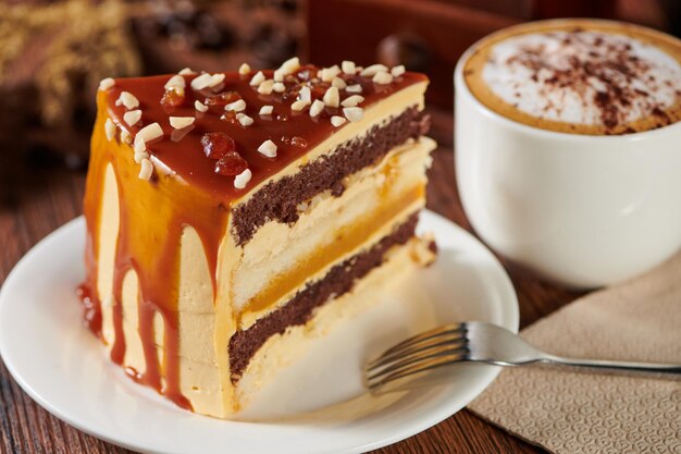 Slice of salted caramel sponge cake on a plate with a cappuccino on a wooden table