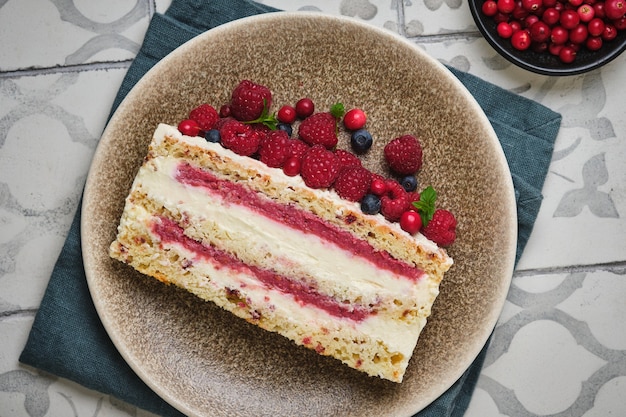 Slice of sponge cake with raspberry filling and coconut cream garnished with fresh wild berries