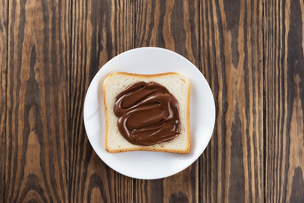 A slice of toast bread with chocolate hazelnut paste in a plate on a wooden table