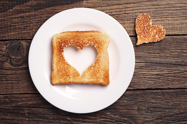 Fetta di pane tostato con forma di cuore ritagliata su fondo di legno