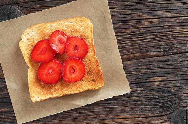 Slice of toasted bread with fresh strawberries on wooden table