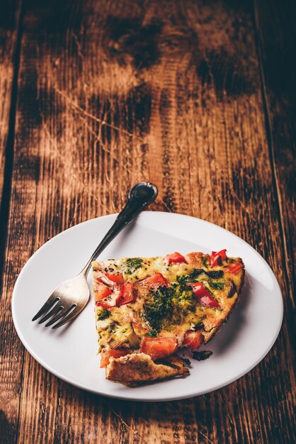 Slice of vegetable frittata on white plate