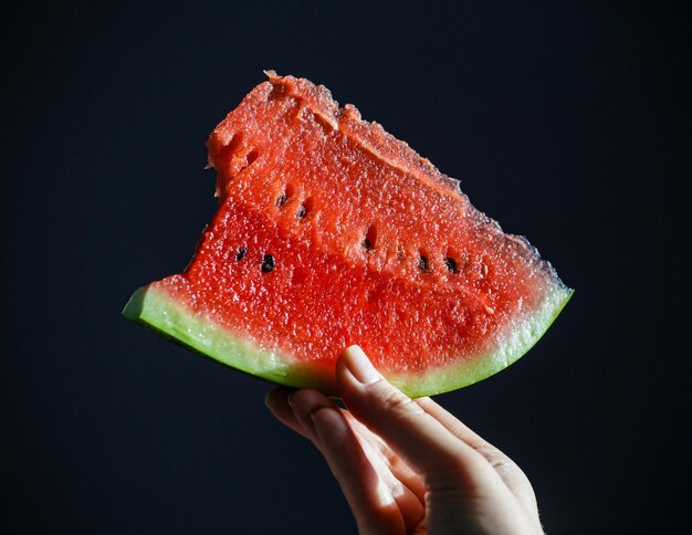 A slice of watermelon in your hand on a dark background A slice of watermelon