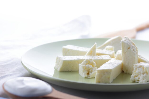 Slice a white soft brynza on a green plate Cheese with cream and wooden cutlery on a light background Closeup of a dairy product