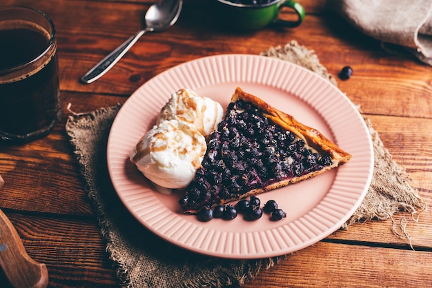 Slice zelfgemaakte Serviceberry Pie en twee scoops van Vanilla Ice Cream op een bord op een houten tafel